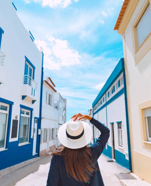 Rear view of a young woman tourist with white hat walking on the narrow streets of south Portugal on a sunny summer day. Summer holiday vacation. High quality photo